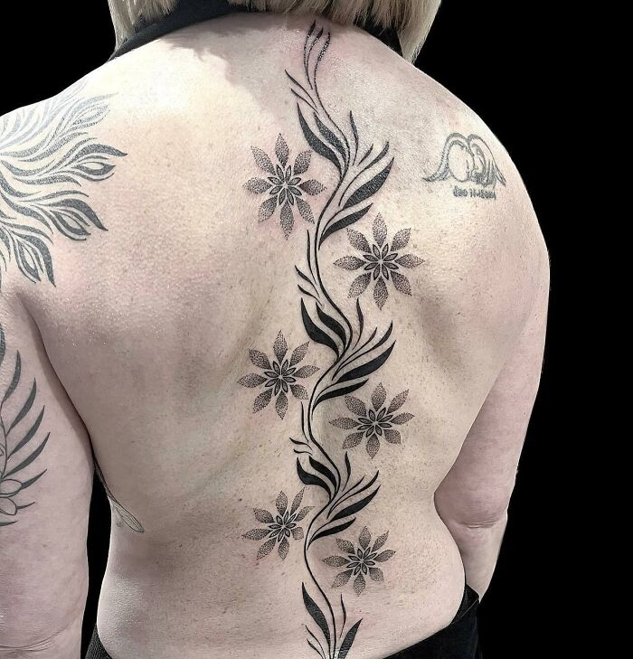Black decorative vine and flowers tattoo on spine
