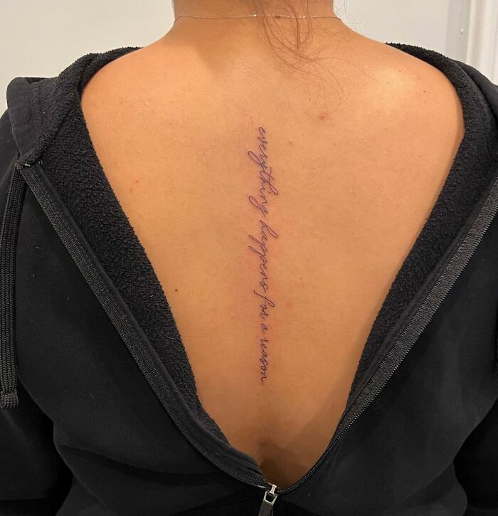 Person with a spine tattoo in cursive font, wearing a black top with an open back.