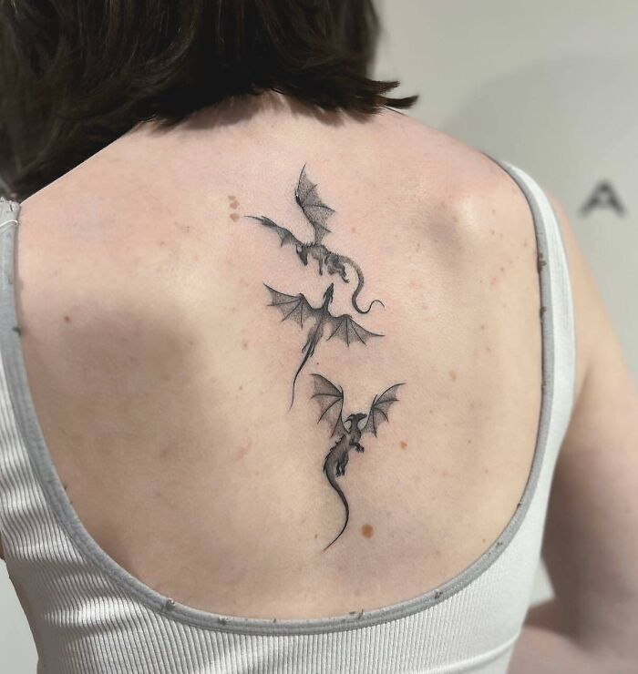 Three dragon spine tattoos on a person's back, showcasing intricate black ink design.