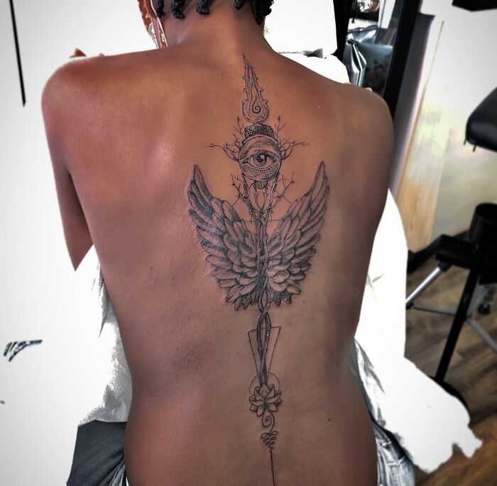 A detailed spine tattoo featuring an eye and wings on a person's back.