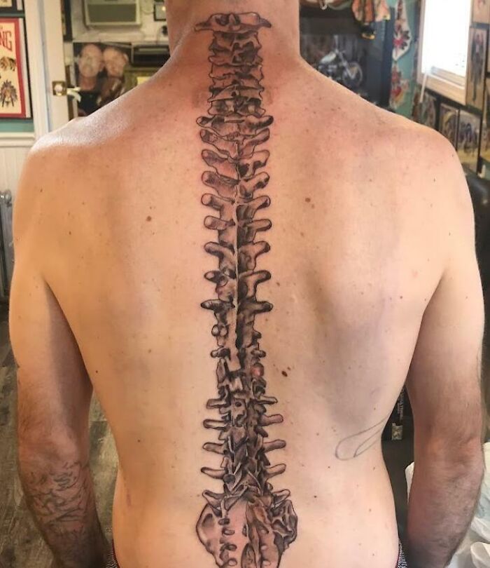 Detailed spine tattoo on a man's back in a tattoo studio setting.