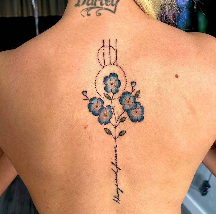 Delicate floral spine tattoo with blue flowers and cursive text.