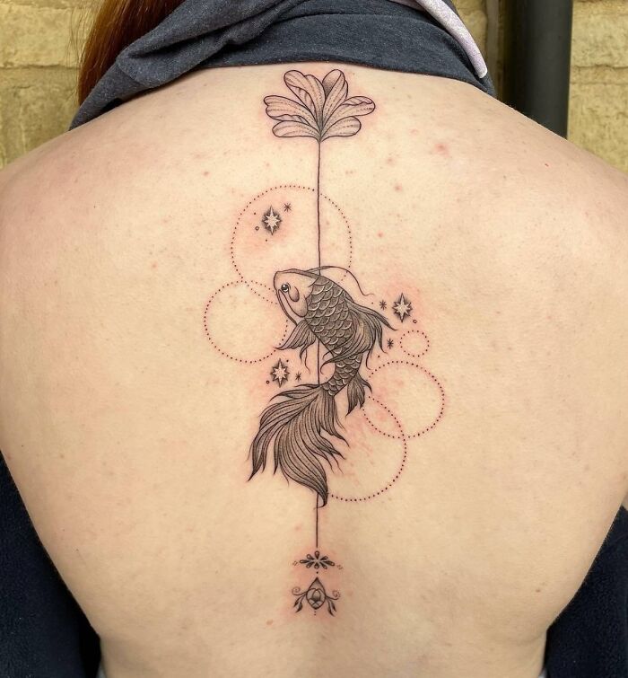 Intricate spine tattoo featuring a koi fish and floral design on a bare back.