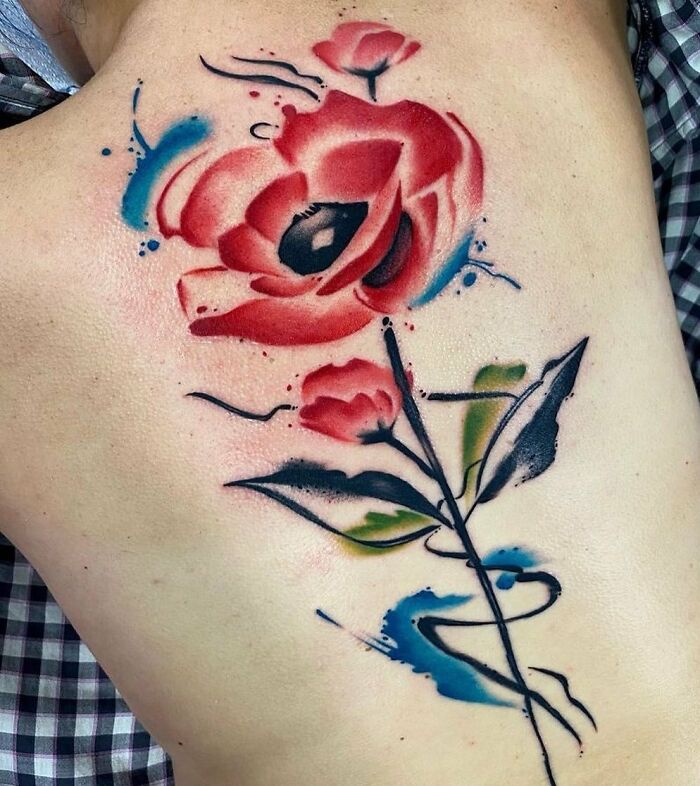 Vibrant floral spine tattoo in watercolor style, featuring red and blue hues.