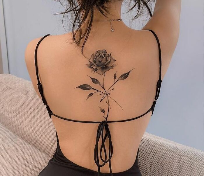 Back view of elegant rose spine tattoo in black ink on a woman's back.