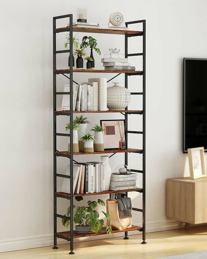 A 6-tier adjustable tall bookcase with wooden shelves and many books and plant pots in it