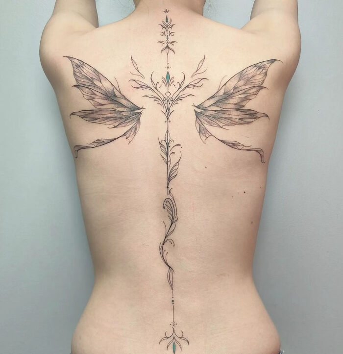 Delicate floral spine tattoo with wing accents on a person's back.