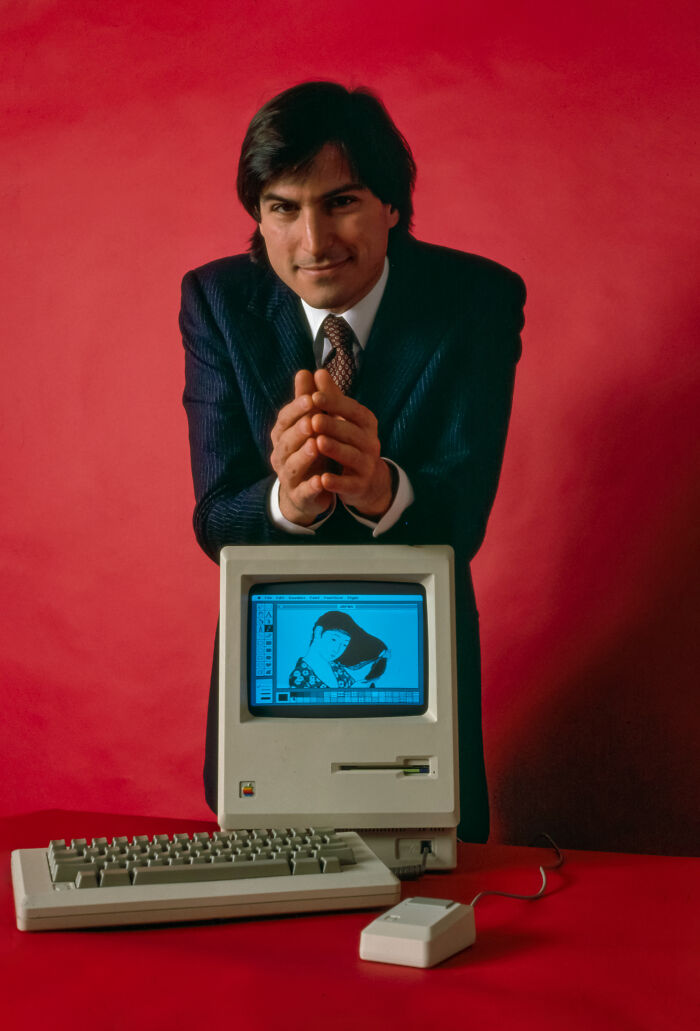 Young Steve Jobs posing next to a computer 