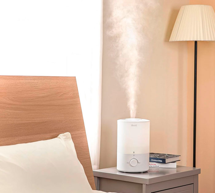 A white humidifier on the bedside table near the bed
