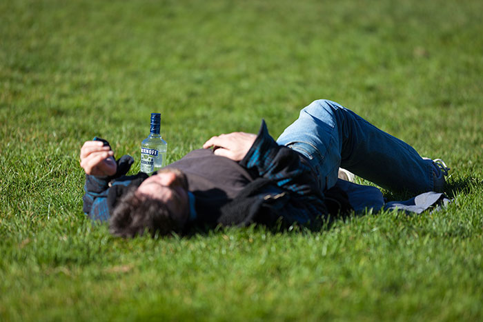 A man laying in the grass with a bottle of alcohol