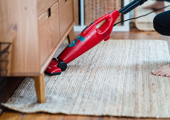 A Person Vacuuming a Carpet Under a Side Cabinet