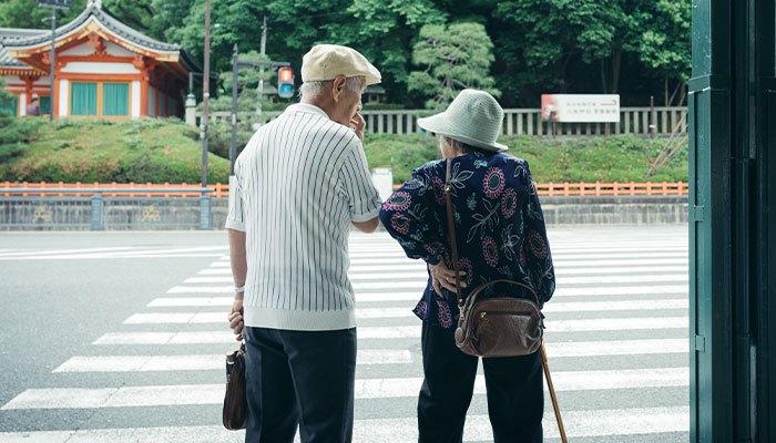 Elderly couple crossing a street, evoking thoughts on human longevity and ancient times linked to dinosaurs. Elderly couple crossing a street, evoking thoughts on human longevity and ancient times linked to dinosaurs.