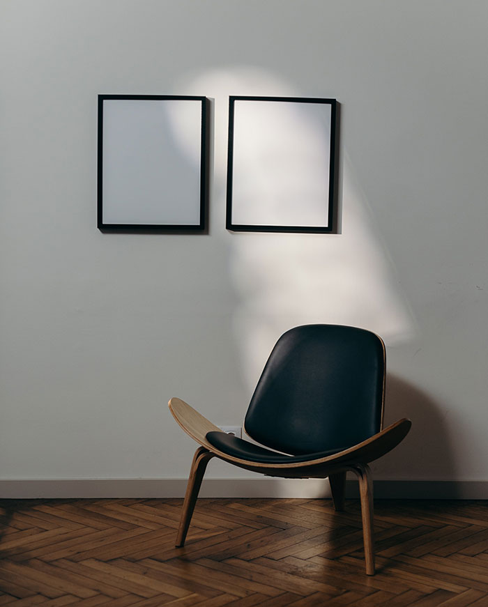White frames hanging on the wall and black wooden chair on the ground.