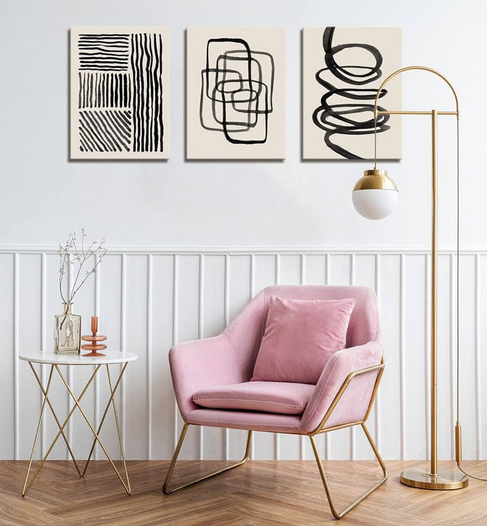 Abstract art pictures hanging on the wall above pink chair.