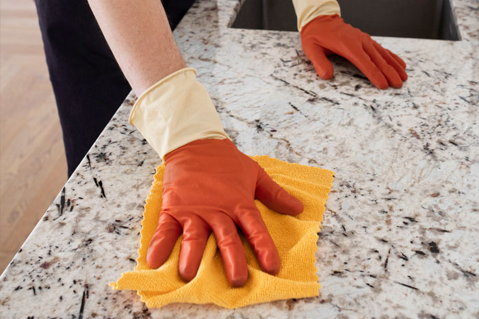 A person wearing gloves and cleaning a white granite countertop.