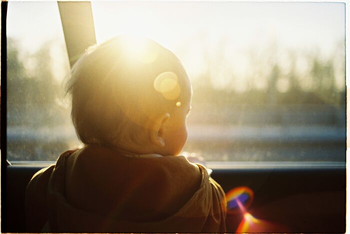 baby standing next to a sunny window 