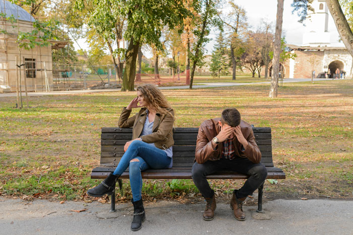 Couple experiencing family drama, sitting apart on a park bench with tense expressions. Couple experiencing family drama, sitting apart on a park bench with tense expressions.