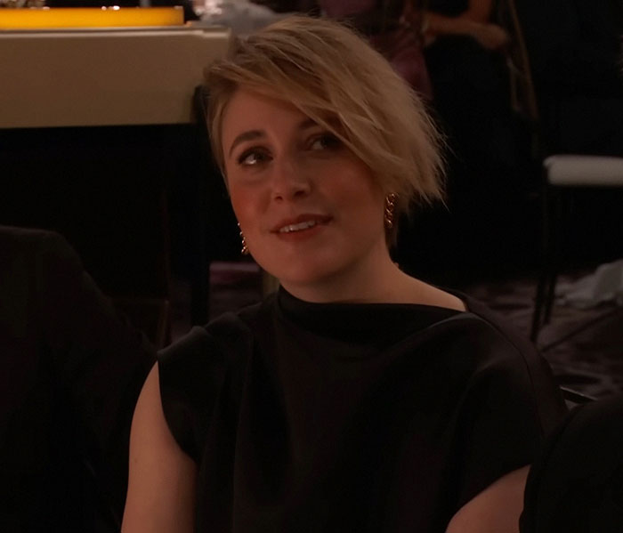 Greta Gerwig in a dimly lit setting, wearing a black outfit, responding to a statement with a thoughtful expression. Greta Gerwig in a dimly lit setting, wearing a black outfit, responding to a statement with a thoughtful expression.
