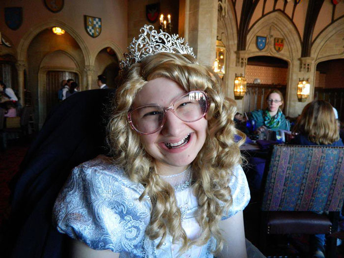 Person in costume with curly wig and tiara sitting in a themed restaurant. Person in costume with curly wig and tiara sitting in a themed restaurant.