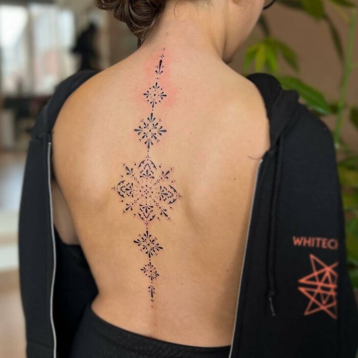Delicate black ornamental tattoo on woman’s back