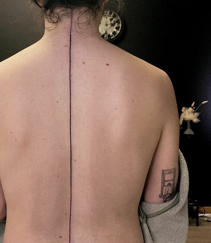 Minimal black vertical line tattoo on spine