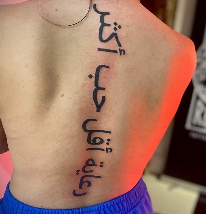 Black Arabic lettering tattoo on spine