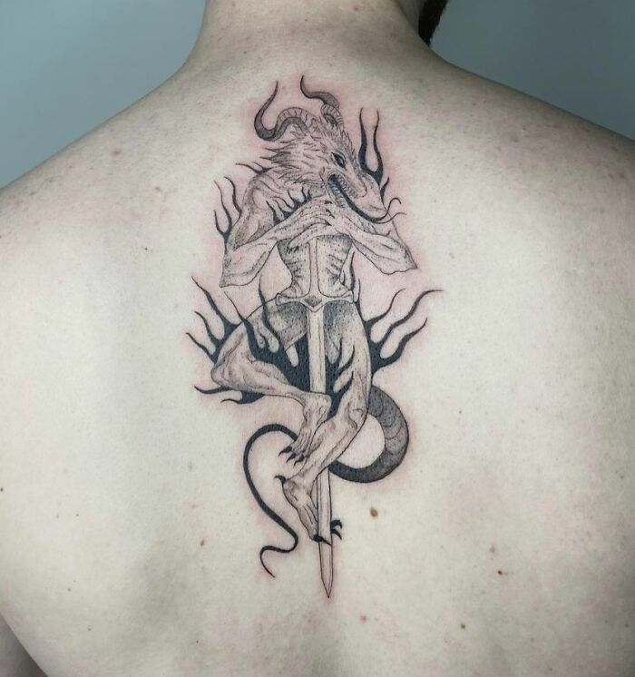 Demon on sword tattoo on man’s upper back