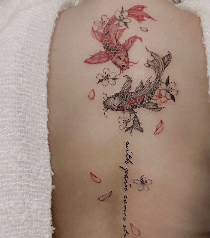 Two koi fish, lettering, and small flowers tattoo on the back