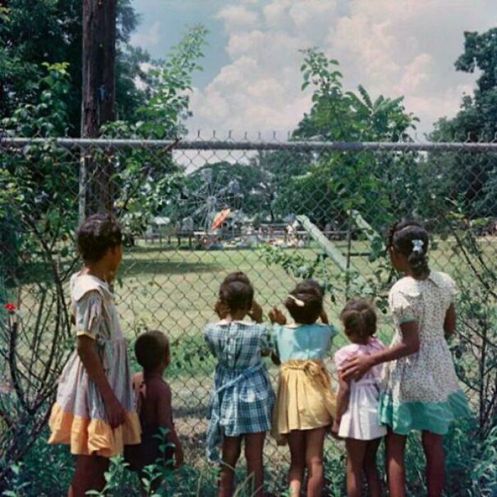Niños negros mirando a niños blancos jugando en un parque solo para blancos, 1956