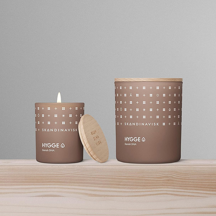 Two scented candles are on a wooden surface and one is lit