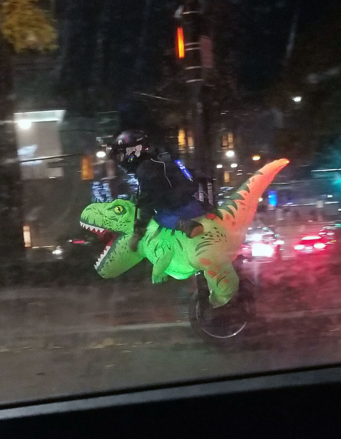 Un tipo en monociclo disfrazado de dinosaurio