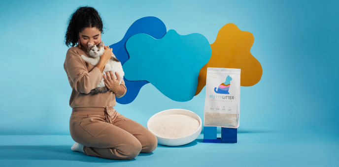 Woman cuddling a cat beside a bag of cat litter with abstract blue and yellow shapes in the background. Woman cuddling a cat beside a bag of cat litter with abstract blue and yellow shapes in the background.