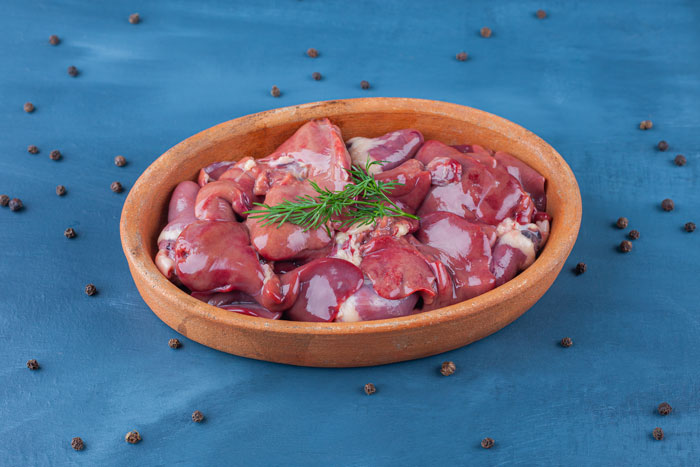 Bowl of raw chicken meal ingredients on a blue background, garnished with fresh herbs. Bowl of raw chicken meal ingredients on a blue background, garnished with fresh herbs.