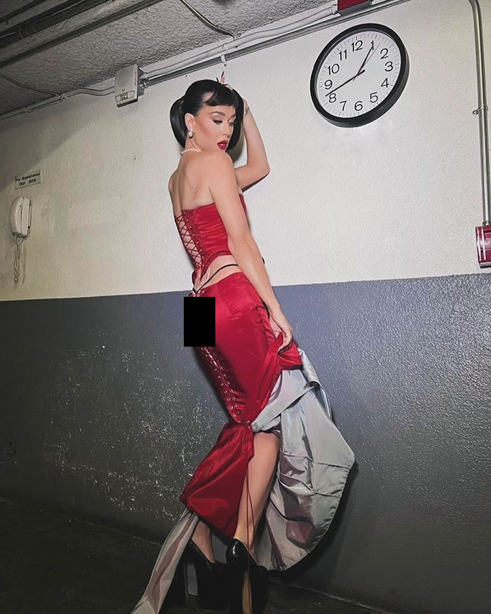 Katy Perry in a red dress poses in a hallway under a clock, showcasing a butterfly tattoo. Katy Perry in a red dress poses in a hallway under a clock, showcasing a butterfly tattoo.