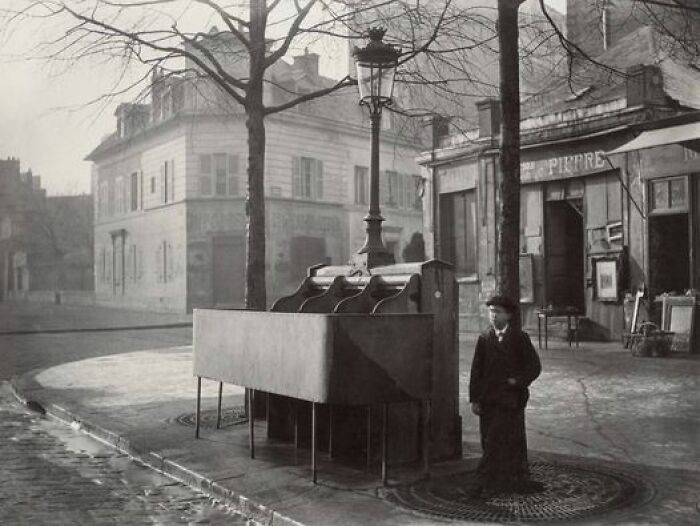 A Boy Stands Near A Pissoir, One Of The Many Outdoor Urinals Installed On The Streets Of Paris Starting In The Mid-19th Century