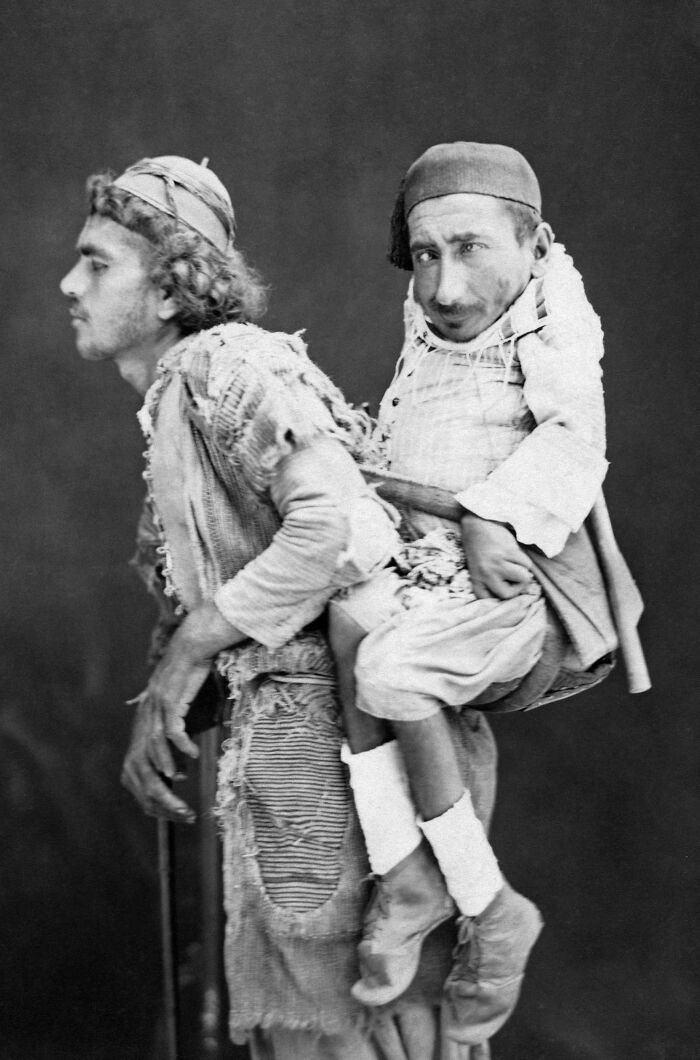 Muhammad, un musulmán ciego, cargando con su amigo cristiano Samir, que sufre enanismo y parálisis. Damasco, 1889