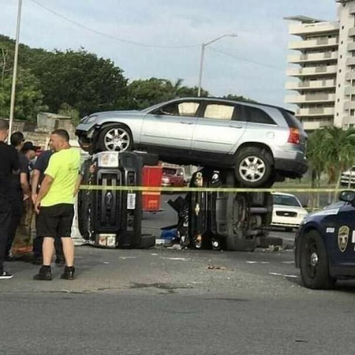 Two cars involved in a wild coincidence accident with a silver car stacked on top of overturned vehicles, police on scene.