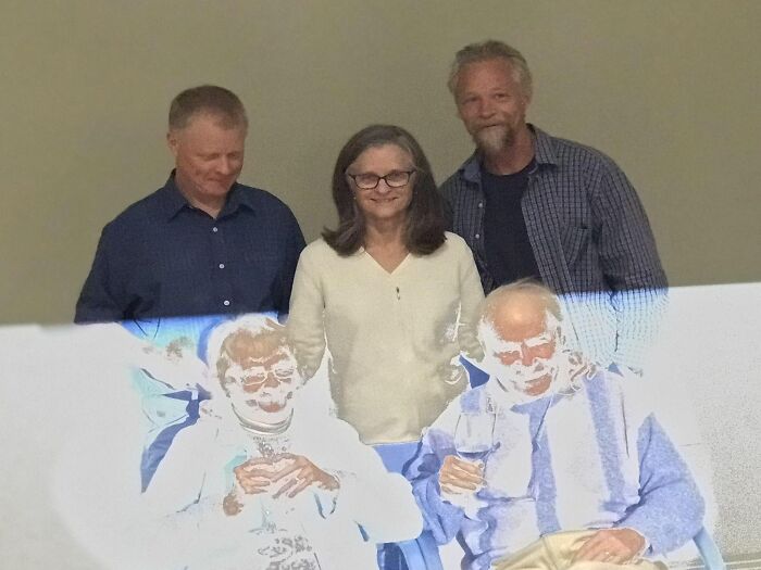 Four people posing with a projected image creating a coincidence effect, showing two older figures holding glasses.