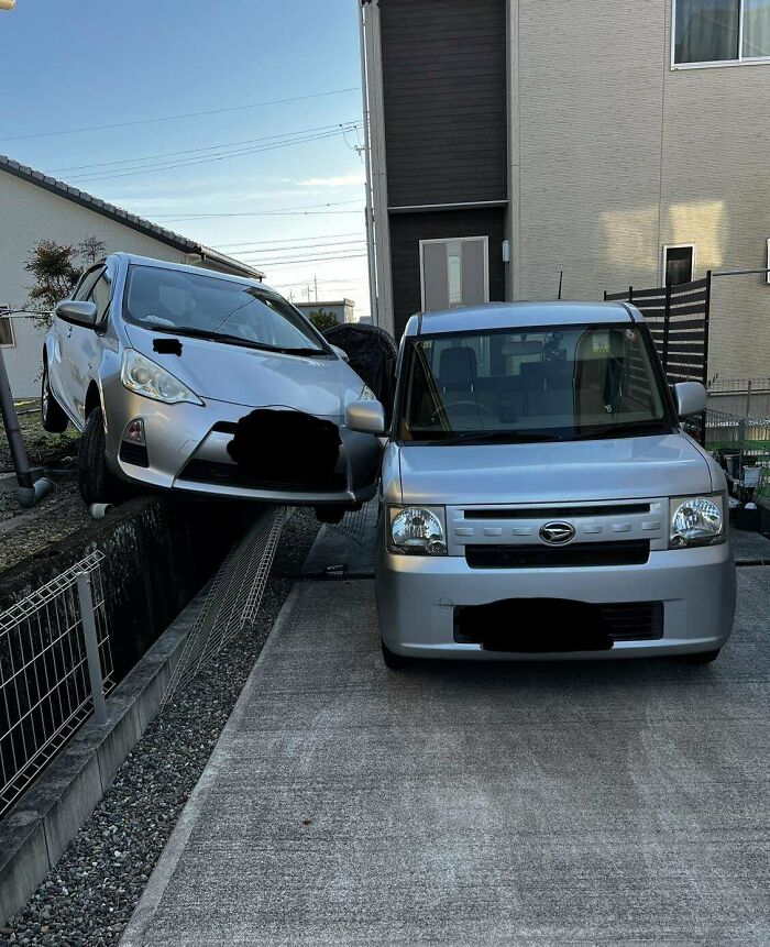 Two silver cars in a driveway, one oddly perched on a fence, showcasing wild coincidences caught in photos.