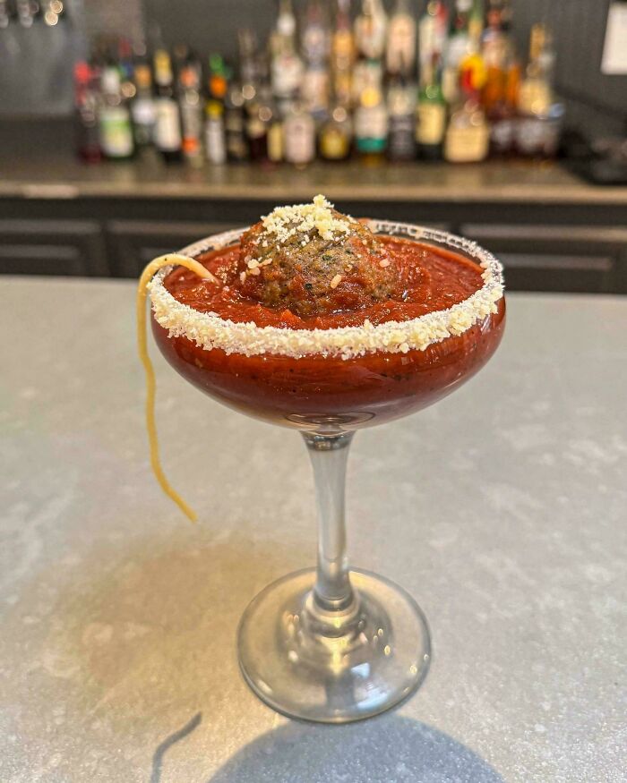 Cocktail glass filled with spaghetti sauce, meatball garnish, and Parmesan rim in a creative ridiculous food serving idea.