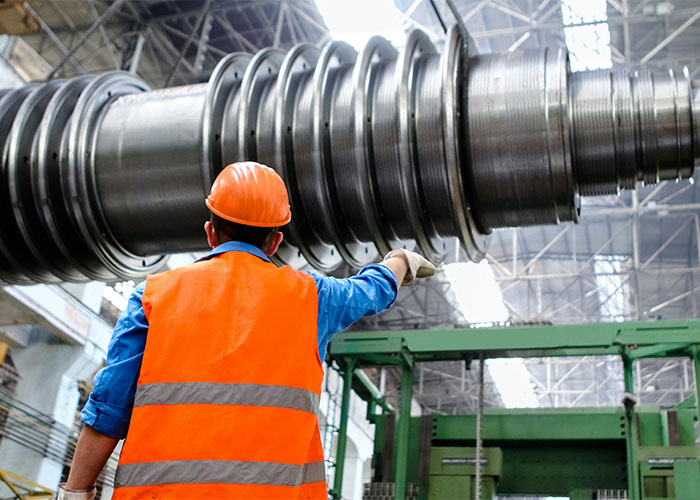 Machinist in an orange vest operating heavy machinery in a factory setting. Machinist in an orange vest operating heavy machinery in a factory setting.