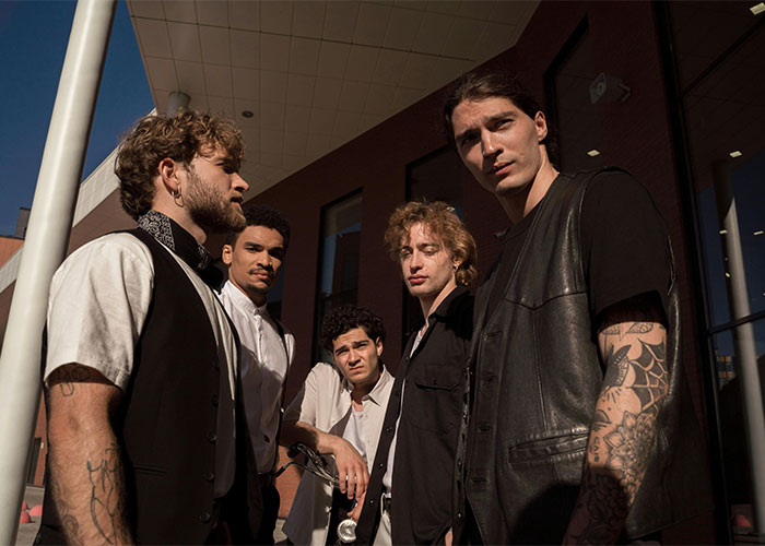 Five men standing together outside a building, one with visible arm tattoos. Five men standing together outside a building, one with visible arm tattoos.