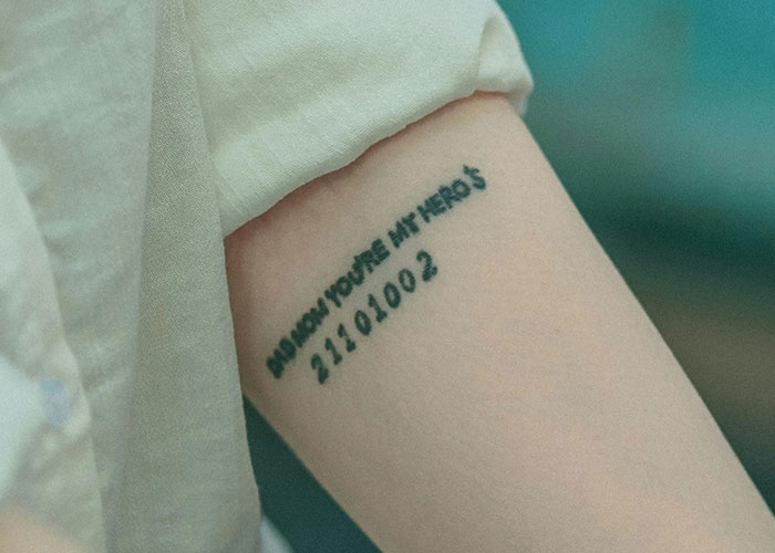 Tattooed arm with numbers and text under a white sleeve, linked to a grandmother's story. Tattooed arm with numbers and text under a white sleeve, linked to a grandmother's story.