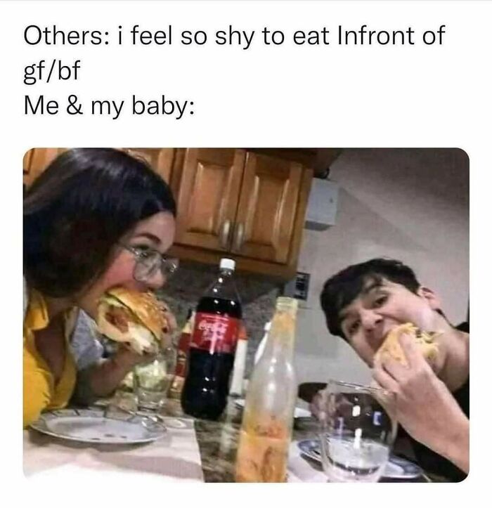 Couple eating large sandwiches casually at a kitchen table, illustrating relatable random memes about shared experiences.