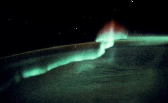 View of aurora borealis creating a colorful glow over Earth from space in the 1990s.