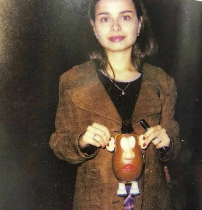 Woman in a brown coat holding a toy, capturing the essence of nineties nostalgia.