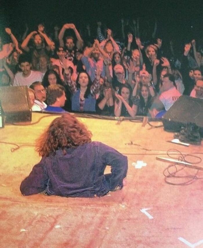 Musician reclining on stage at a 90s concert, crowd cheering energetically, capturing the essence of nineties nostalgia.