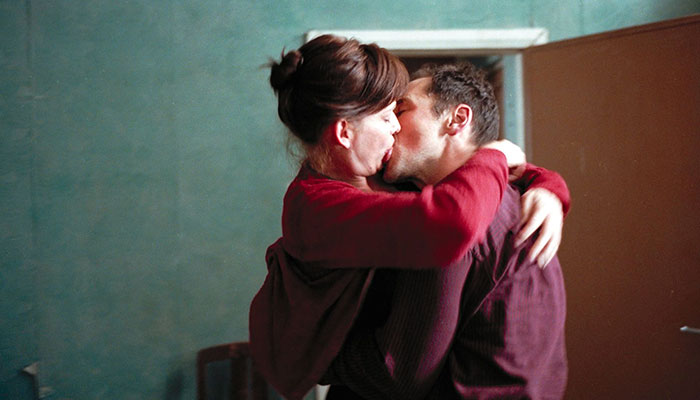 Movie stars embracing passionately while filming an intimate scene in a room with a blue wall. Movie stars embracing passionately while filming an intimate scene in a room with a blue wall.