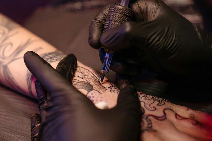 Tattoo artist working on an arm, highlighting study linking tattoos to cancer risk, with focus on lymphoma concerns. Tattoo artist working on an arm, highlighting study linking tattoos to cancer risk, with focus on lymphoma concerns.