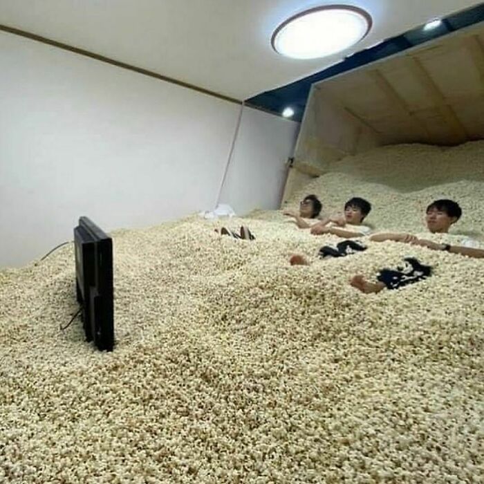 Three people lying in a room filled with popcorn, watching a TV, showcasing random and cringe humor.